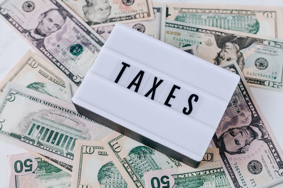 A sign stating taxes on top of a pile of money.